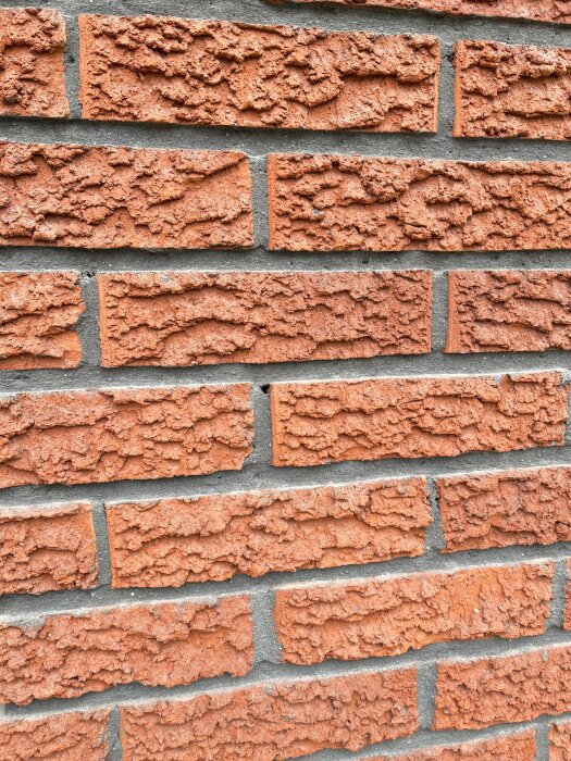 Röd tegelstensvägg med grov textur, murad med grå fog.
