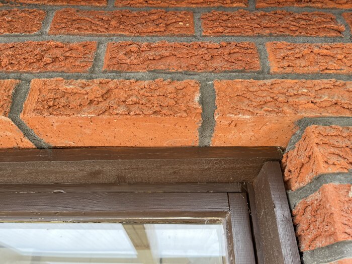 Rödbrun tegelvägg ovanför ett brunt fönsterkarm, med gråaktigt murbruk, från ett hus byggt 1974 i Sörmland.