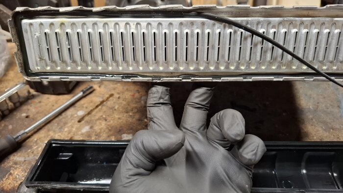 Gloved hand pointing to a radiator where the gasket is misaligned in two spots, showing the cause of a leak between the cell block and plastic end.