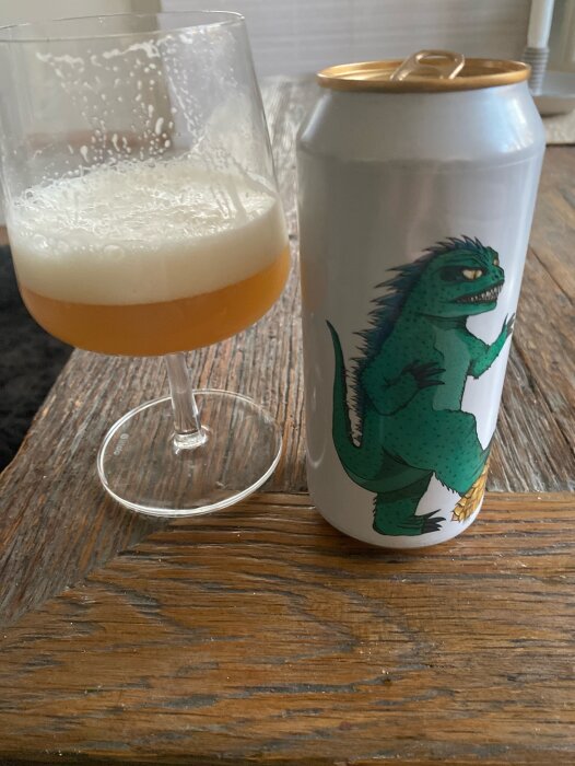 En halvtom ölglas bredvid en burk med illustration av en grön dinosaurie.