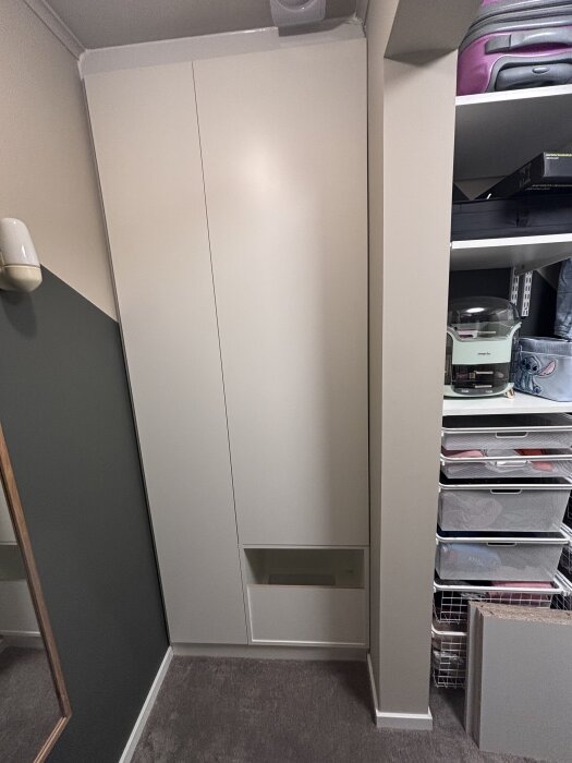 Vitt tvättnedkastskåp monterat i ett rum, med hyllor och förvaringslådor på sidan.