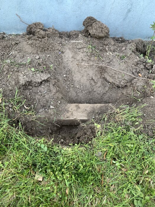 Metallbalk under jord nära husets grund, omgiven av gräsmatta och uppgrävd jord.