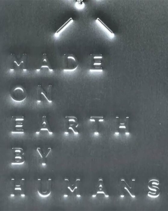 Prägling med texten 'Made on Earth by Humans' på metallgrå yta.