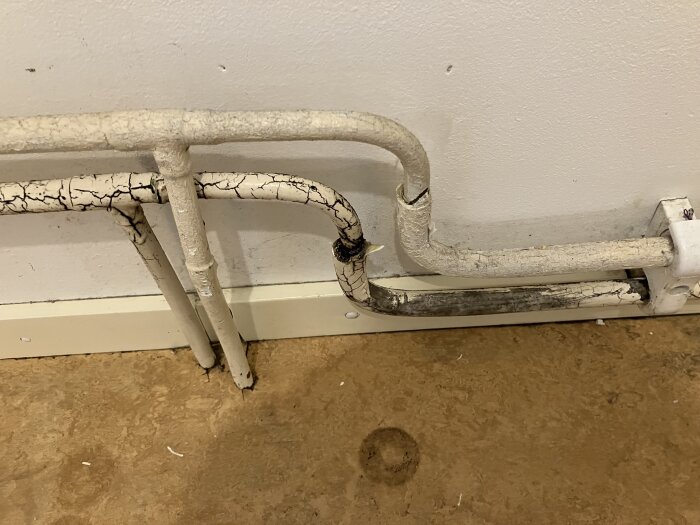 Spruckna vita rör med mörka fläckar längs rören nära en vägg och golv. Besökaren frågar om mögel och dess påverkan på rören.