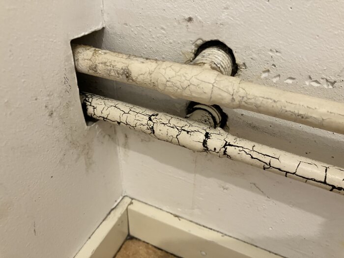 Rör i ett vägghörn med sprucken färg och mörka fläckar.