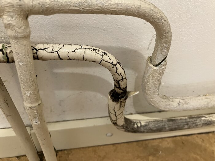 Rör med sprucken vit färg och mörka fläckar, eventuellt mögel, mot en vit vägg.