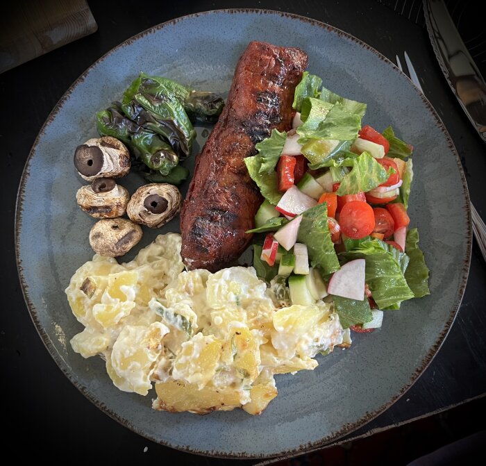 Grillad köttbit med potatisgratäng, grillade champinjoner, padrones och en färgglad sallad med salladslök, tomat, paprika, gurka och rädisa.