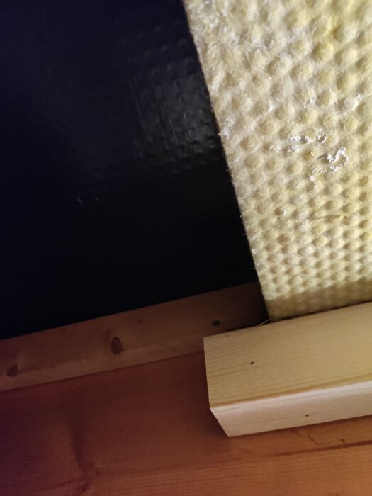 Närbild på tunn isoleringsskiva monterad på träram, bredvid svart yta.