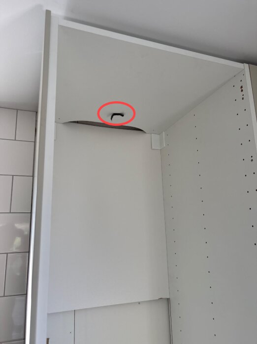 Ett Ikea-skåp inuti ett kök med vit kakelvägg, visar planerad ventilationsplats markerad med röd cirkel.