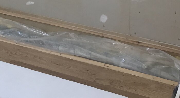 Bild på träpanel med genomskinlig plast och isolering under, i ett kök före ombyggnad.