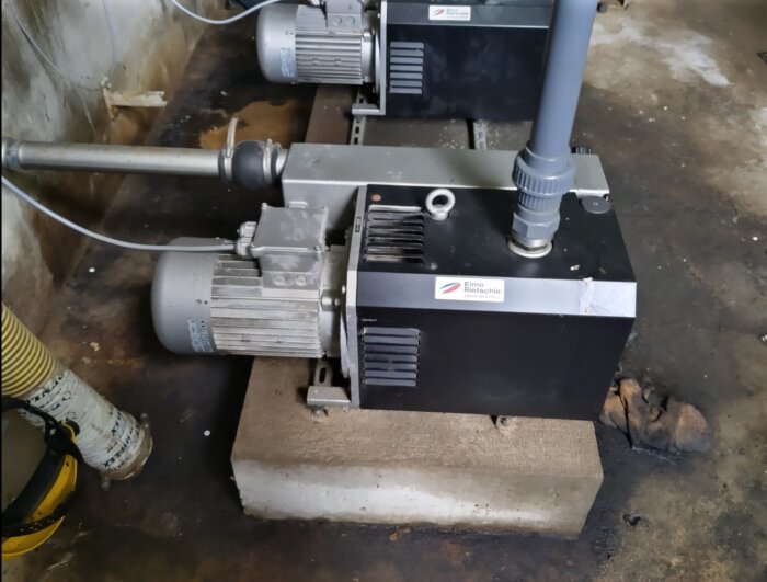 Två Elmo Rietschle vakuumpumpar placerade på en cementplatta i en industriell miljö.