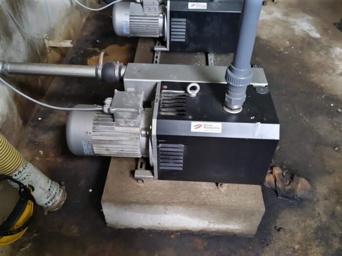 En vakuumpump från märket Elmo Rietschle placerad på en betongplatta i ett garage eller verkstad.