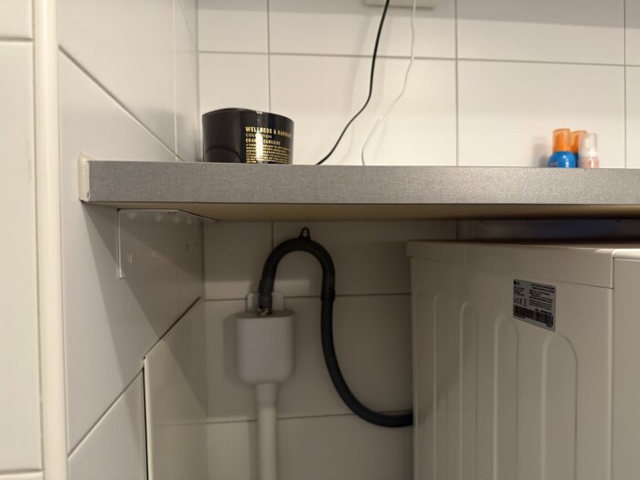 Bänkskiva i badrum ovanför tvättmaskin med synligt stöd och rör, samt flaskor och burk på skivan.