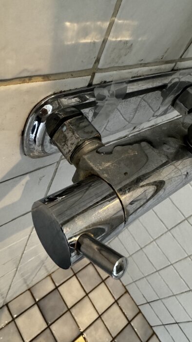 Duschblandare monterad på kaklad vägg med synliga kopparfärgade rör och en lös hylsa, verkar svår att demontera.