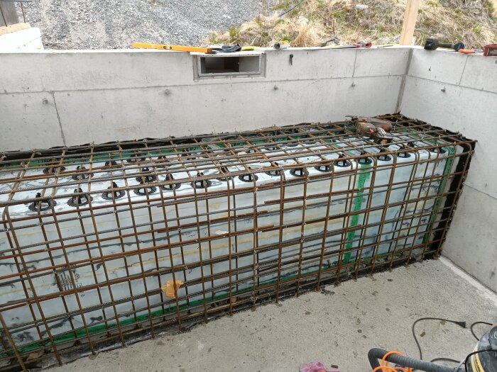 Armeringsjärn på plats för en betongbänk, omgiven av betongväggar och cellplastblock, med verktyg liggande ovanpå.