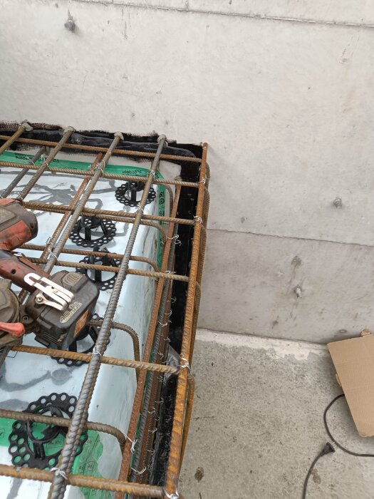 Armeringsjärn placerade på en byggarbetsplats för gjutning av bänk, med cellplast och distanser synliga under nätet på en konkret yta.