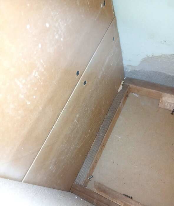 Fläckar och mögel på en plywoodpanel i ett kök, synligt bakom skåp, med en unken och frän lukt. Huset är från 1959.