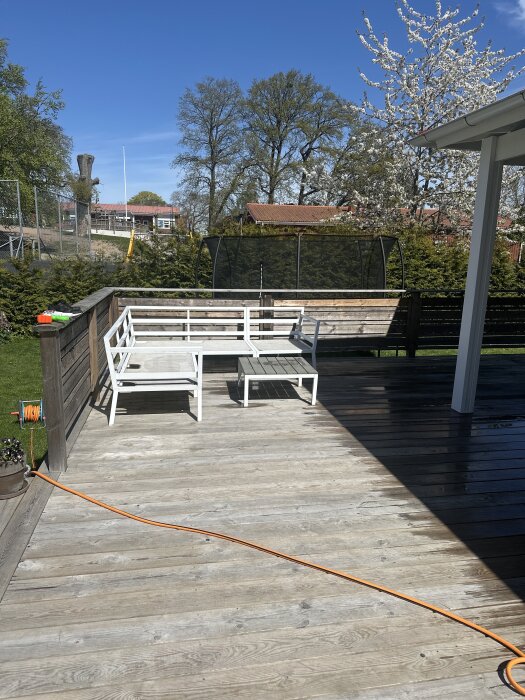 Stor altan med vita utemöbler, i bakgrunden en inhägnad studsmatta, omgiven av träd och buskar.