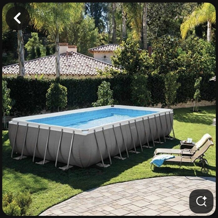 Rektangulär ovanmarkspool placerad på gräsmatta, omgiven av träd och buskar, med solstolar bredvid.