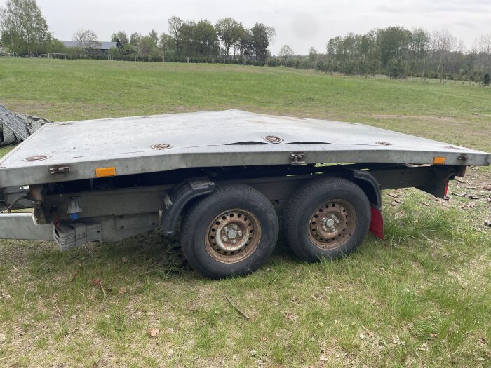 Släpvagn utan ram, uppställd på gräs, med två hjul synliga.