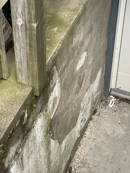 En sliten källartrappa med lossad puts och fuktfläckar på sidan. Trästolpe synlig till vänster.