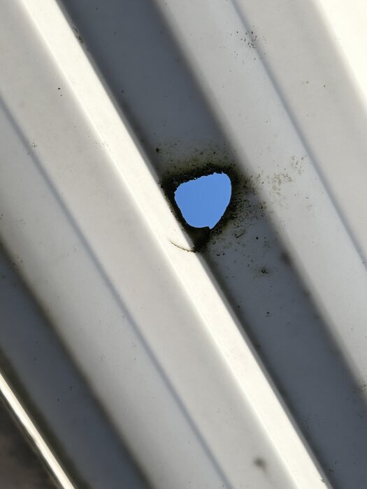 Hål i ett vågformat plasttak på uteplatsen, med blå himmel synlig genom hålet.