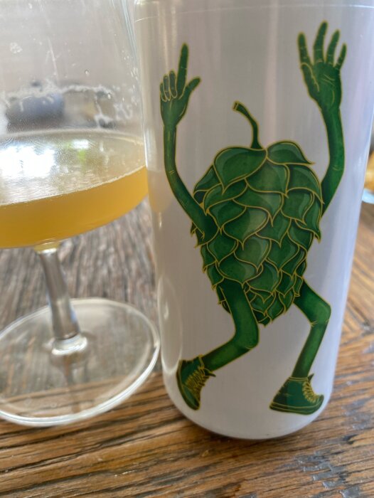 En ölburk med en tecknad humlekotte med ben och armar bredvid ett glas halvfullt med öl på ett träbord.