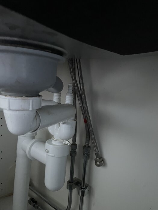 Rör och anslutningar under köksvask för installation av diskmaskin, inklusive vattenrör och avlopp.