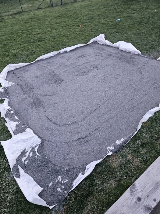 Stenmjöl utlagt på markduk i en gräsmatta som förberedelse för ett byggprojekt, omgärdat av gräs.