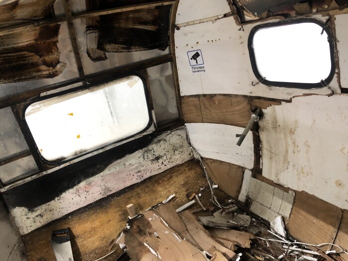 Rivningsarbete i en gammal husvagn, med synliga söndriga golvplankor, trasiga väggar och fönsteröppningar, i processen att renoveras.