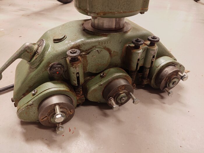 Grön och rostig maskindel med tre lager och bultar, troligen från en mekanisk anordning, synligt smörj- eller synglas till vänster.