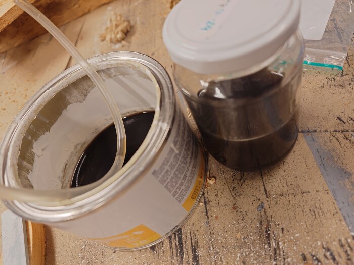 Burk och glasbehållare med mörk olja på ett arbetsbord, med en slang placerad i burken.