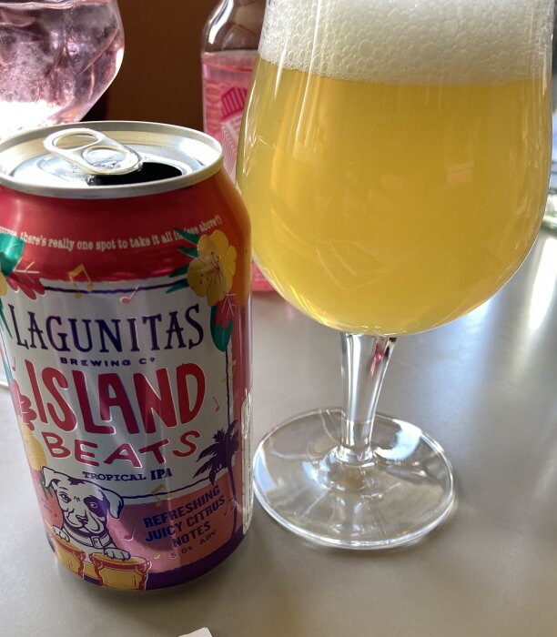 En burk Lagunitas Island Beats Tropical IPA bredvid ett glas med ljus öl på ett bord.