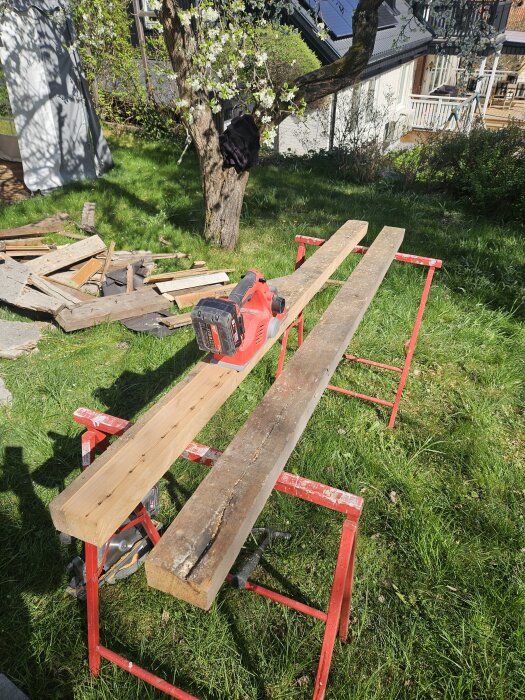 Rivningsvirke återanvänds för ny karm till boddörr. Två plankor ligger på bockar med en eldriven såg ovanpå i en trädgård.