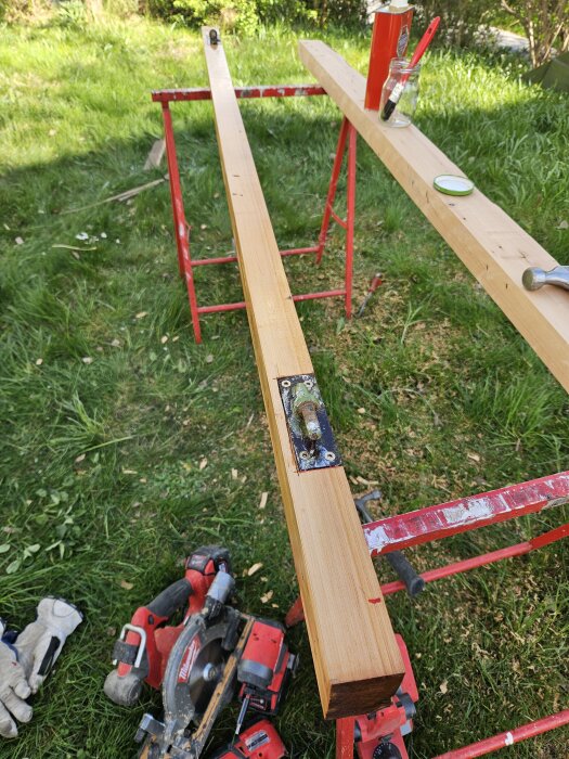 Återvunnet virke för dörrkarm, placerat på bockar i trädgård med verktyg och färg i burk.