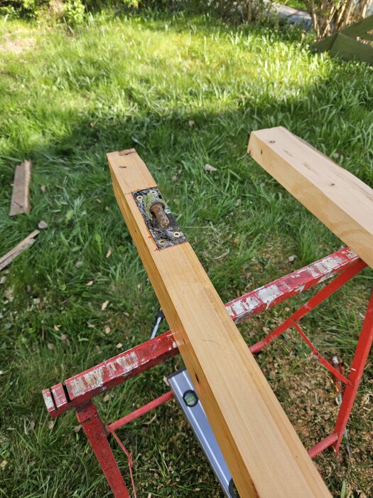 Trästycken i gräs på röd ställning, används för att bygga en ny dörrkarm av återanvänt rivningsvirke.