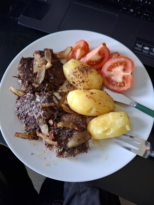 Pannbiffar med stekt lök, kokt potatis och tomater på en tallrik.