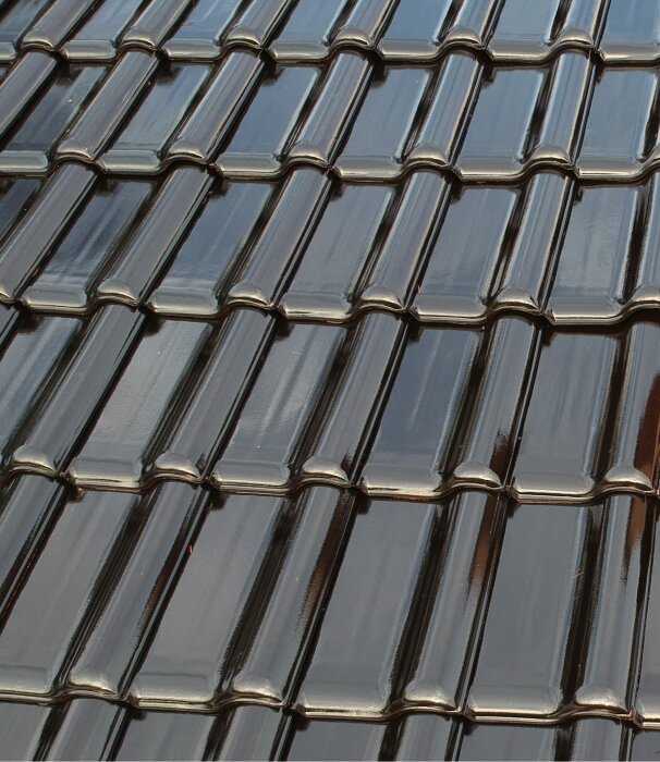 Svarta, helglaserade tegelpannor från Creaton på ett tak, visar en högblank yta som kompletterar en ljus gulmålad fasad.