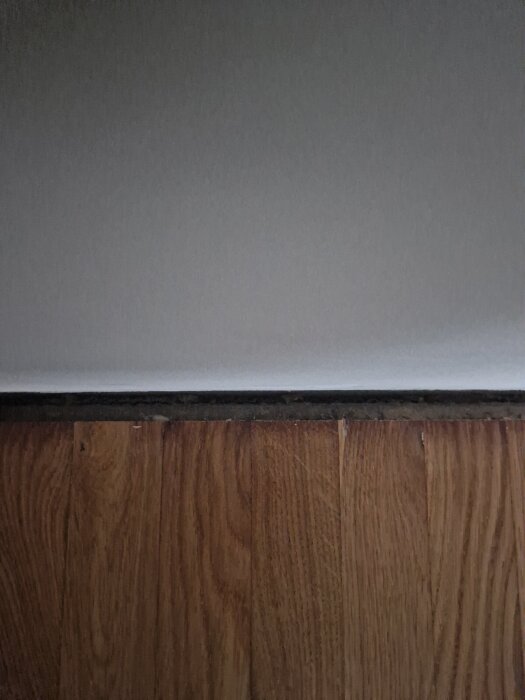 Glipa mellan fiskbensparkett och vägg i ett rum, synlig klyfta som mäts till 1.5 - 1.8 cm.