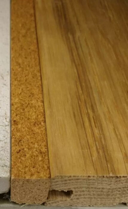Korkremsa och träplanka placerade sidan vid sida, möjlig lösning för att minska glipor mellan golv och vägg i rum med fiskbensparkett.