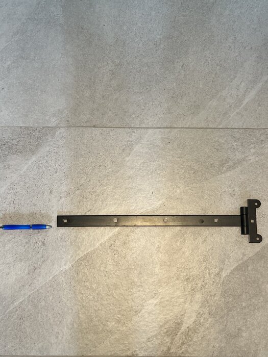 Svart gångjärn och blå penna på grå klinkerbakgrund.