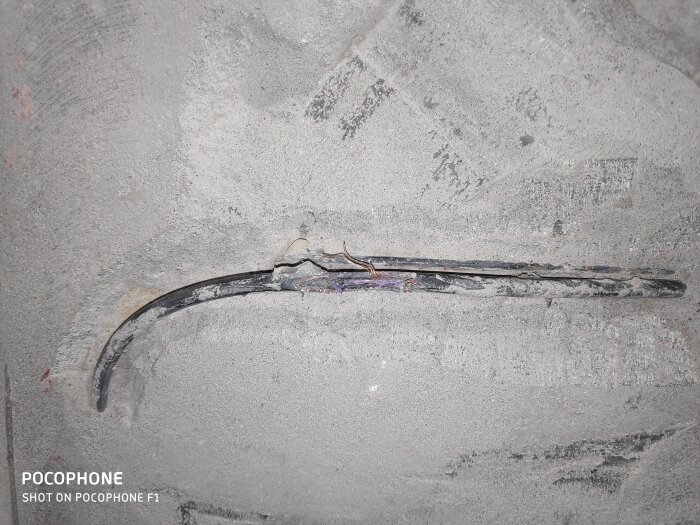 Skadad värmekabel på betonggolv med blottlagda ledningar efter borttagning av gammalt klinker.