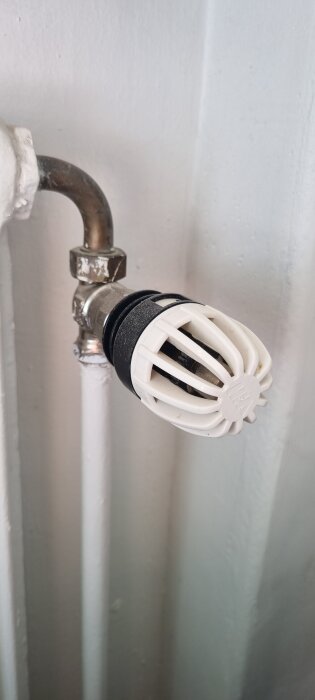 Vitt radiatorreglage som sticker ut från väggen i en äldre fastighet, monterat på ett metallrör.
