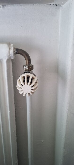 Vitt element med ett äldre reglage som sticker ut från väggen, med ett böjt kopparrör fäst vid reglaget.