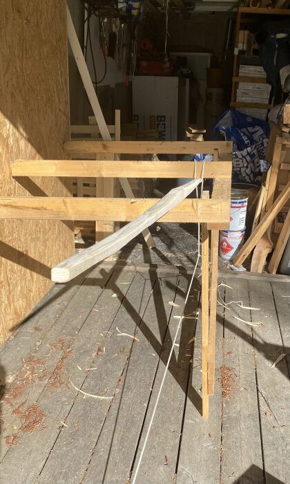 Improviserad täljhäst av trä används för att bearbeta en långbåge; syns med spännband på en sågbänk med verktyg i bakgrunden.