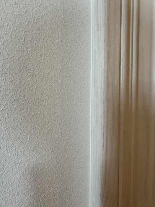 Närbild av en vägg och trälister med nylagd fog synlig emellan. Väggens och listen färg och struktur framgår tydligt.