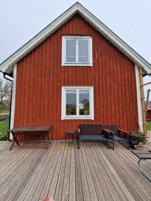 Röd trägavel med två vita fönster, trätrall, bord och stolar. Projekt för ombygd och isolering.
