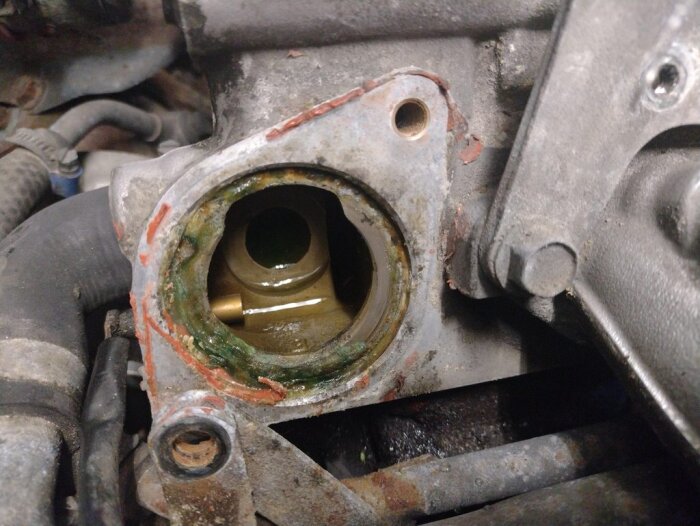 Närbild av en bilmotors termostathus med avlägsnad termostat och spår av silikon runt kanten, där kylvätskeläckage kan ses.