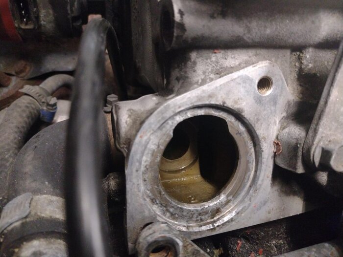 Termostathus på en bil under reparation, utan termostat monterad, med smuts och tecken på läckage runt öppningen.