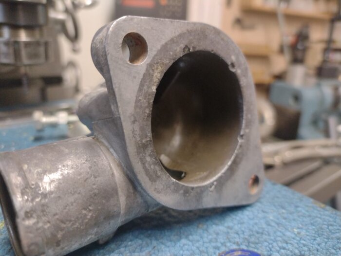 Rostigt termostathus från en Saab på en arbetsbänk, med synliga monteringshål och sliten insida, väntar på rengöring.